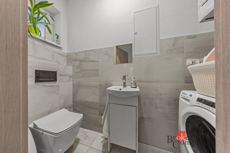 A bathroom in a family house with a toilet and a washing machine, tiled with light tiles.