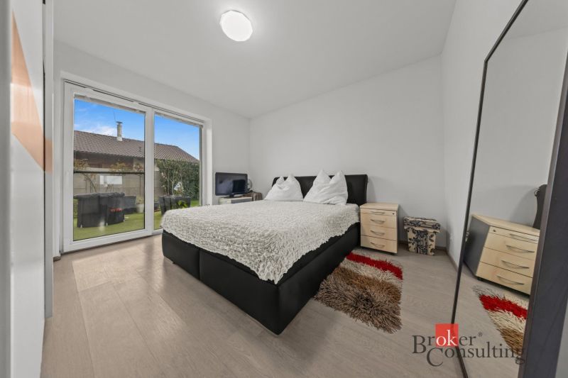 A bedroom in a family house with a French window and a floor with a wooden decor.