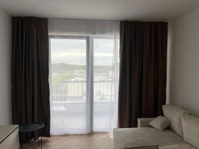 Living room in a two-room apartment with a wooden decor floor and curtains.