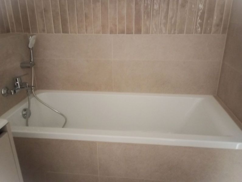 A bathroom with a bathtub and tiles in a 2-room apartment.
