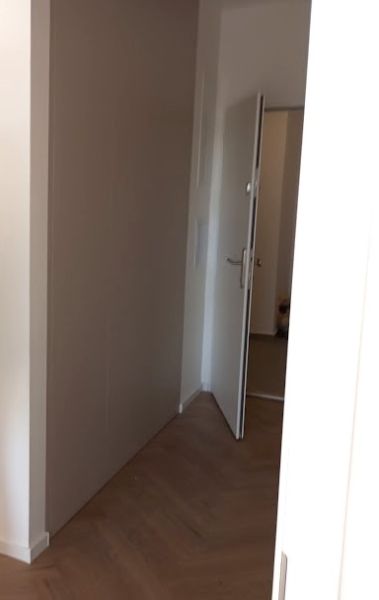A hallway in a 2-room apartment with a wooden decor floor and open doors.