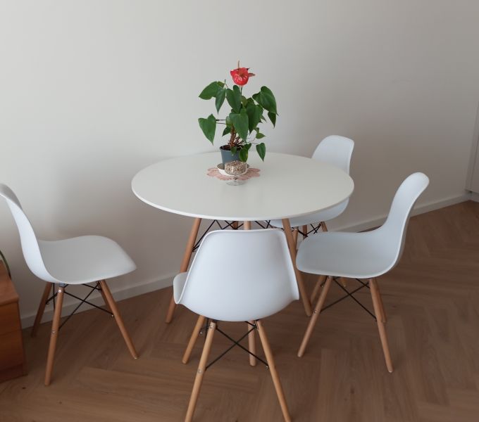A round table with white chairs on a wooden floor in a 2-room apartment.