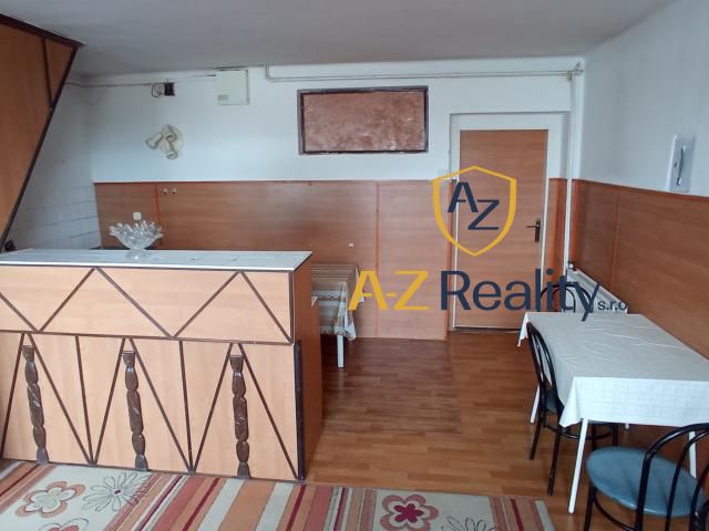 Interior of a building with a kitchen counter, tables, and a wood-patterned floor.