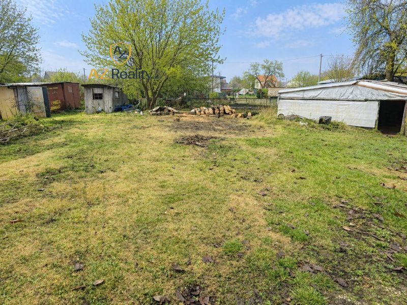 A garden in Nová Osada with trees, wood, and simple shelters.