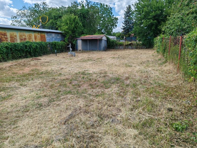 Gardens in Komárno with a lawn, trees, an older gazebo, and fencing.