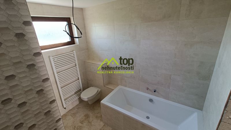 A bathroom in a family house with a bathtub, tiles, and a window for natural light.