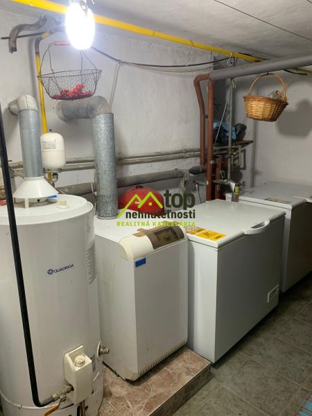 A boiler room in a family house with a boiler and a furnace, white walls, a basket on the piping.
