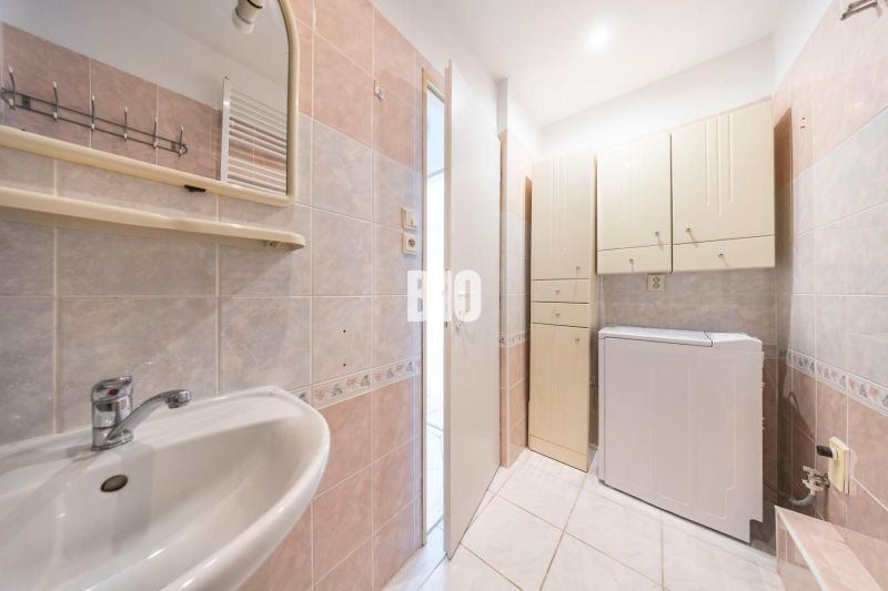 A bathroom in a 2-room apartment with a washing machine, mirror, and cabinets for storage.