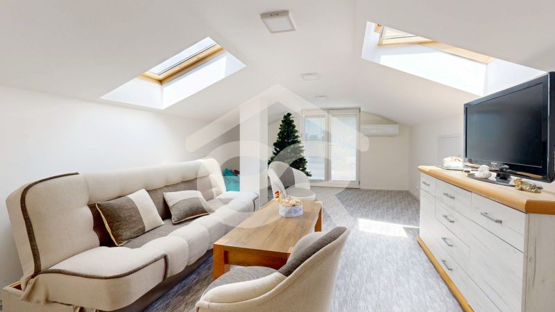 An attic room in a family house with a skylight, sofa, dresser, and television.