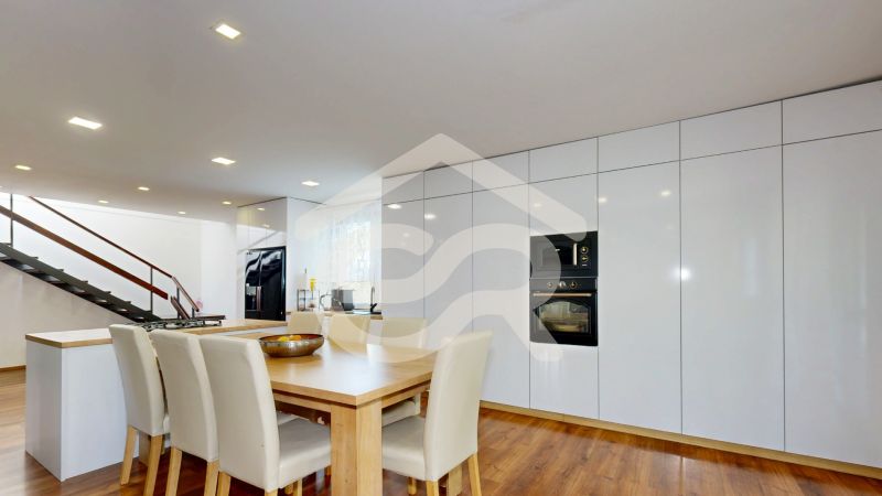 A kitchen in a family house with white furniture, a wooden decor floor, and a staircase.