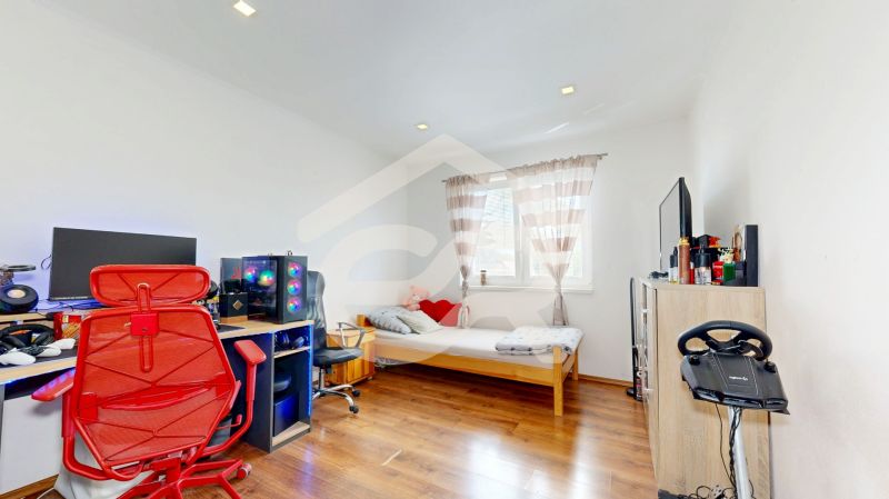 A room in a family house with a computer, a bed, and a wooden decor floor.