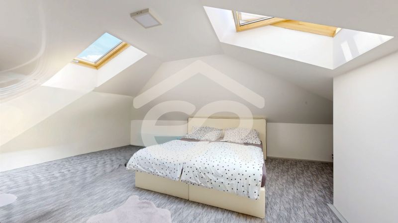 Attic bedroom in a family house with a bed under skylights and a floor with a wooden decor.