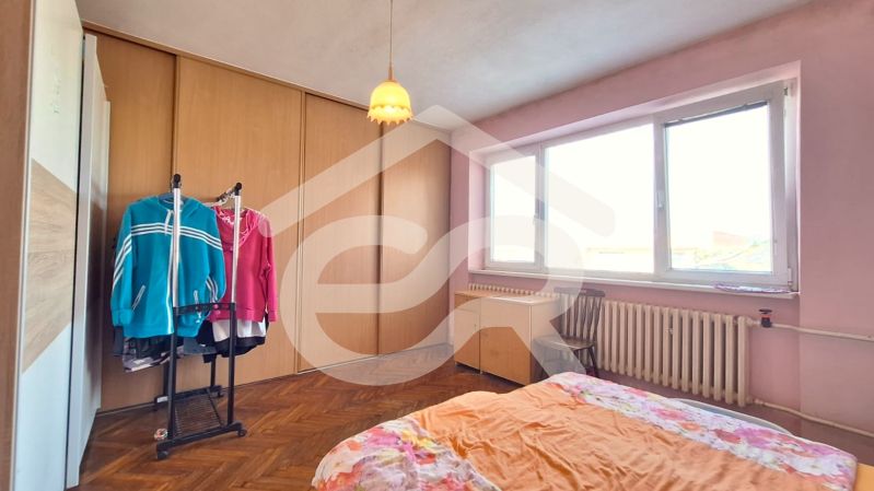 Bedroom in a family house with wood-patterned flooring, pink walls, and a wardrobe.