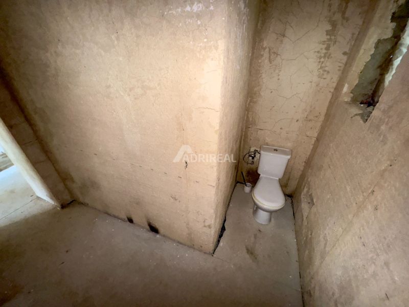 A toilet in an unfinished bathroom of a family house with damaged walls.