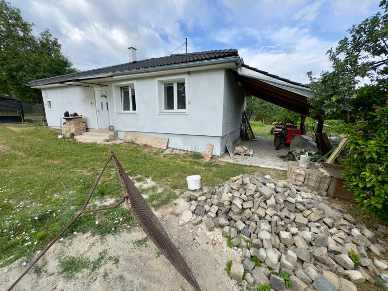 A family house in Ružiná with an unfinished facade and a shelter, surrounded by greenery.