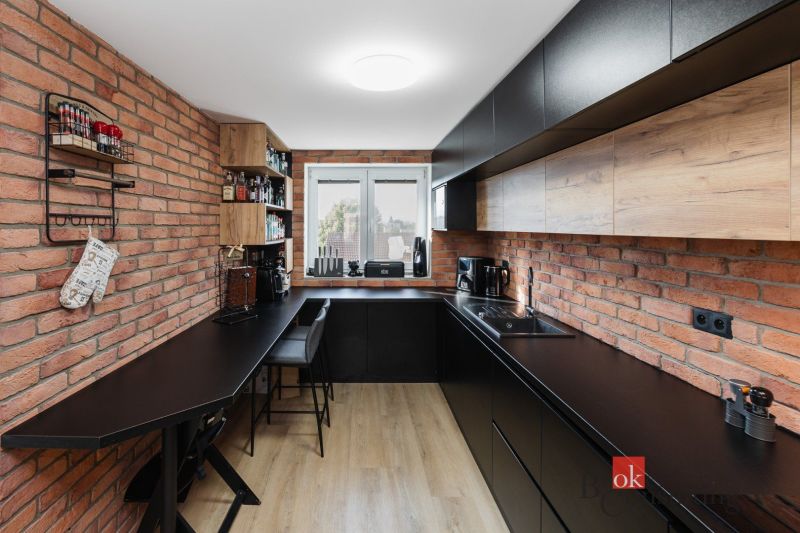 A kitchen with brick walls, black cabinets, and wood-patterned flooring in a two-room apartment.