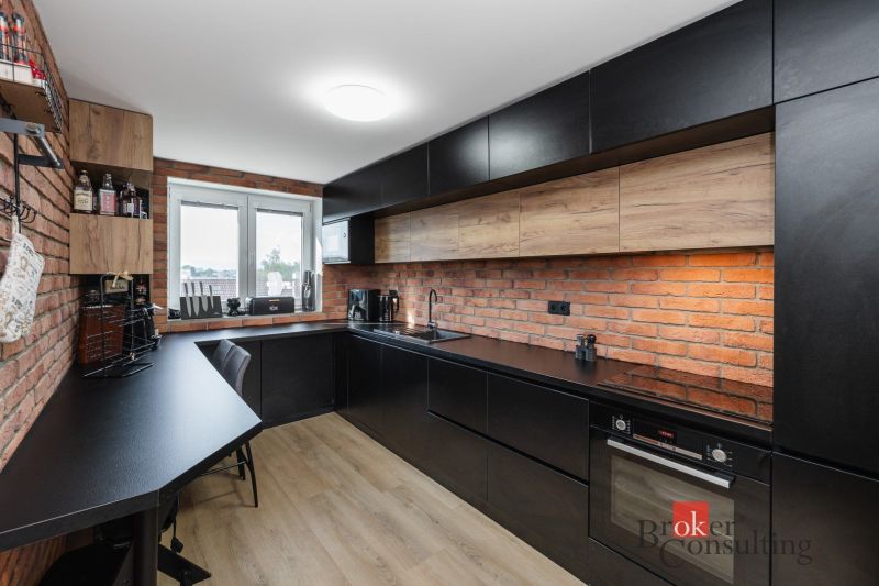 A kitchen with a brick wall, black cabinets, and a wooden decor floor in a 2-room apartment.