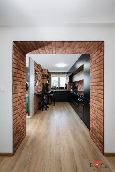 Brick kitchen with black cabinets and wood-patterned flooring in a two-room apartment.