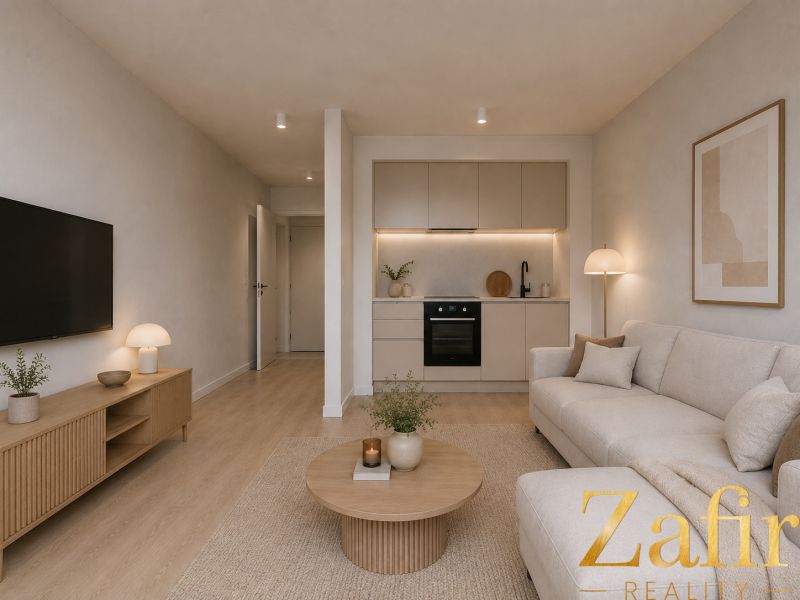 Living room of a studio apartment with wood-patterned flooring, a television, and a kitchenette.