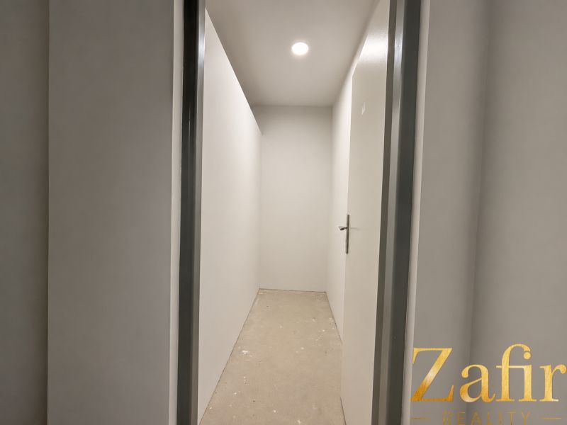 A narrow hallway with white walls and closed doors in a one-room apartment.