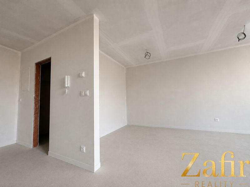 White interior of a 1-room apartment with an empty room and uninstalled light fixtures.