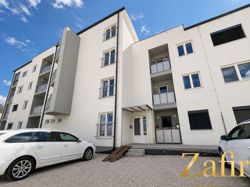 The exterior of an apartment building in Piešťany with a parking lot and white cars in front of a 1-bedroom apartment.