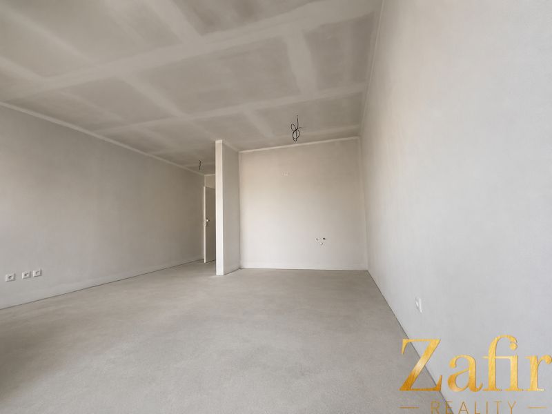 A spacious room with neutral walls and light flooring in a studio apartment.