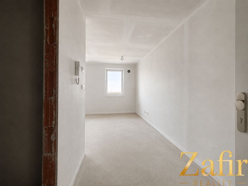 An empty interior of a one-room apartment with white walls and a concrete floor.