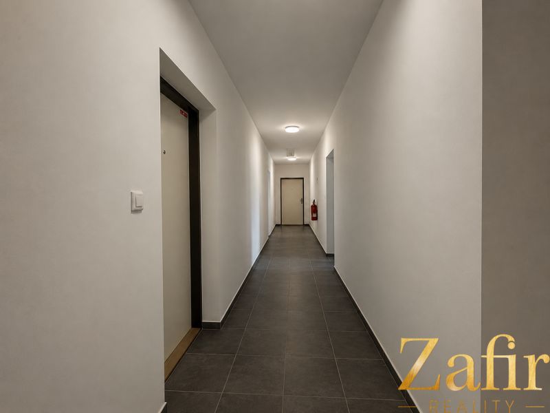 A corridor with white walls and tiles leading to the door in a studio apartment.
