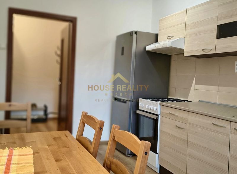 A kitchen in a studio apartment with a wooden table, a refrigerator, and a gas stove.
