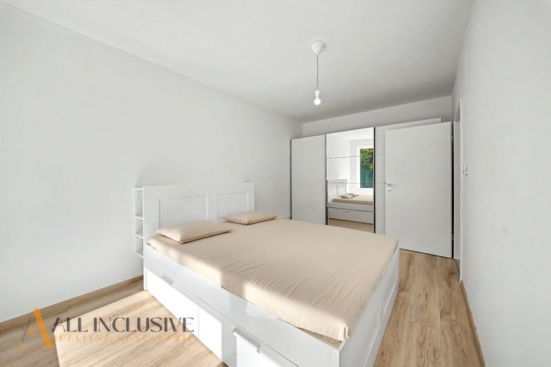 A bedroom in a two-room apartment with a wood-patterned floor and white furniture.