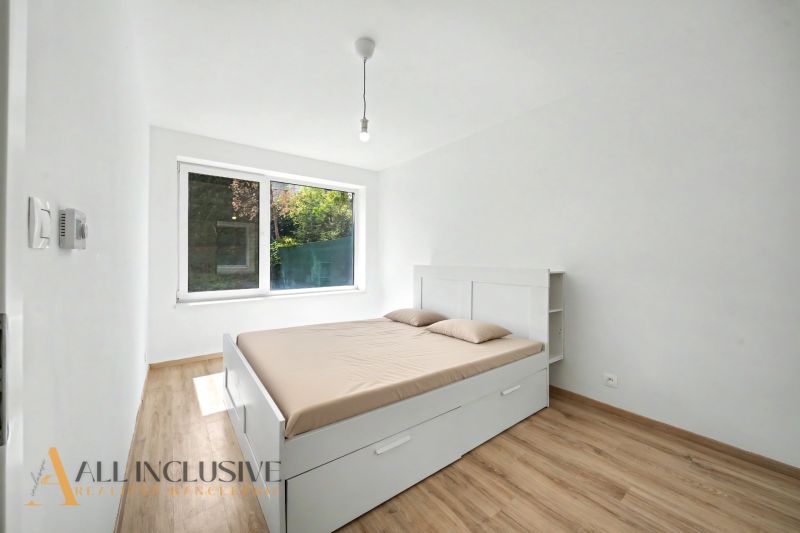 A bedroom with wood-patterned flooring, a large window, and a white bed in a two-room apartment.