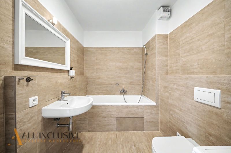 A bathroom in a 2-room apartment with a bathtub, a mirror, and beige tiles.