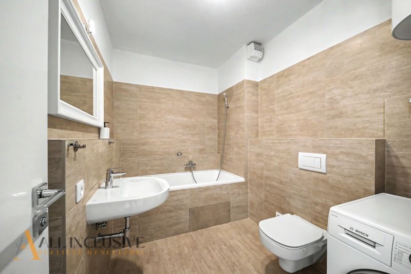 Bathroom in a 2-room apartment with a bathtub, sink, and washing machine, tiled.