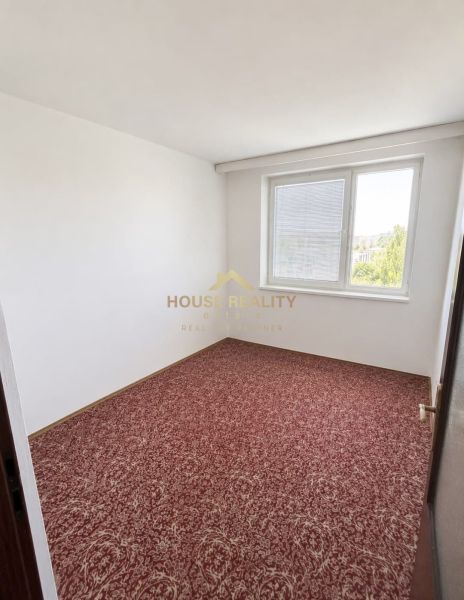 A room in a three-room apartment with a carpeted floor and a large window.