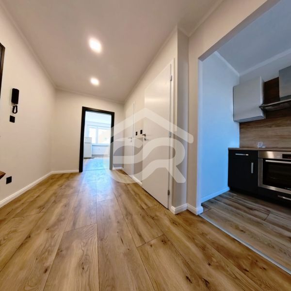 A hallway in a 3-room apartment with a wooden decor floor and an entrance to the kitchen.