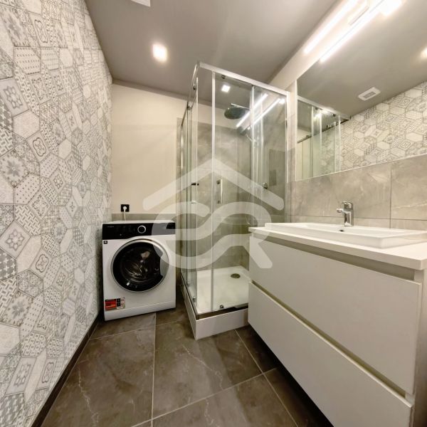 A bathroom in a 3-room apartment with a washing machine, shower, and sink.