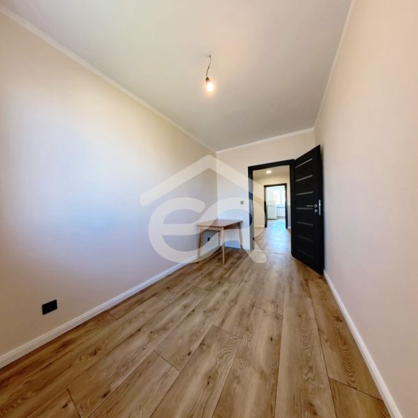 A room with a wooden decor floor in a 3-room apartment with a table and a light bulb.