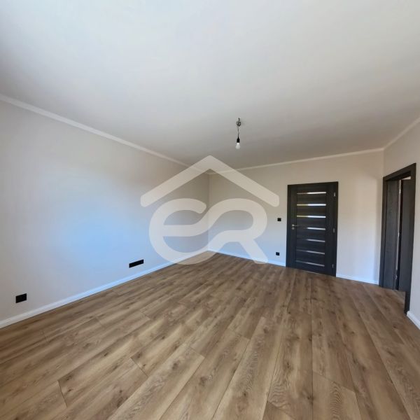 An empty room with a wooden floor and dark doors in a 3-room apartment.