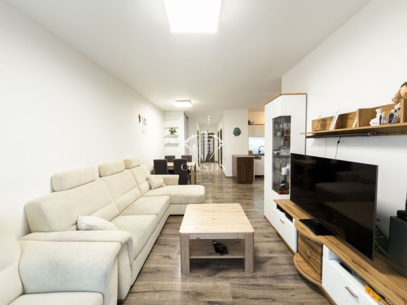 Living room in a 3-room apartment with a wooden decor floor, cream sofa, and TV.