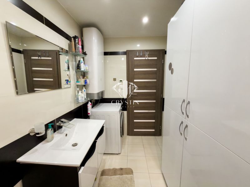 A bathroom in a 3-room apartment with a sink, mirror, cabinets, and a washing machine.