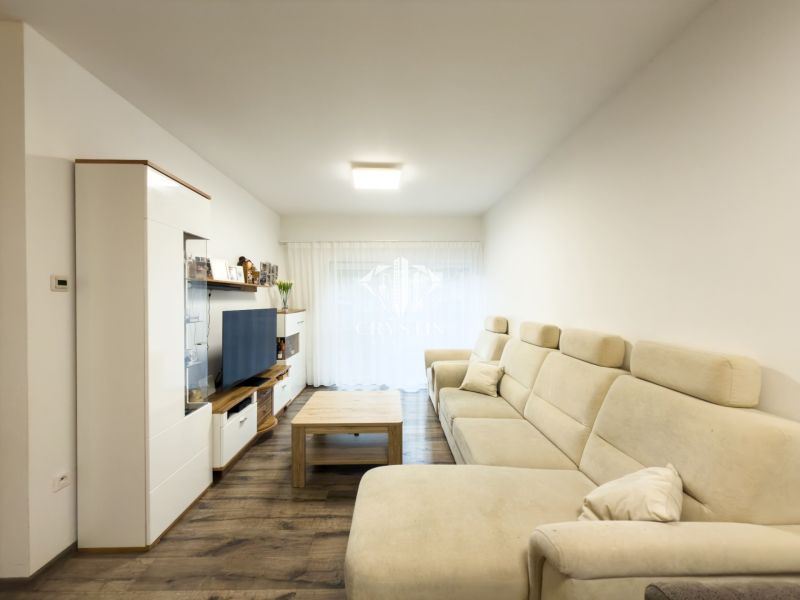 Living room in a 3-room apartment with a light sofa, wooden decor flooring, and a TV stand.