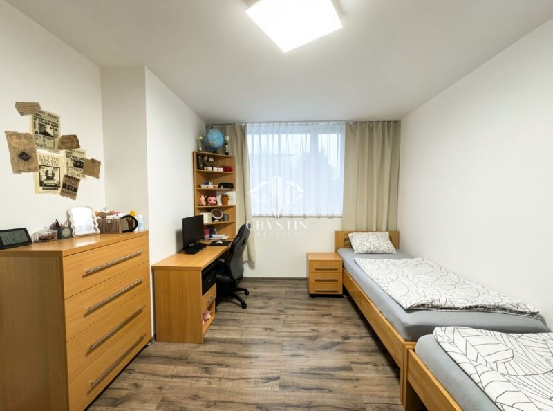 A bedroom in a 3-room apartment with a wood-decor floor, two beds, and a desk.
