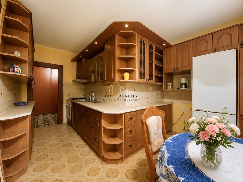 The kitchen of a 4-room apartment with a wooden decor, flowers on the table, cabinets, and appliances.