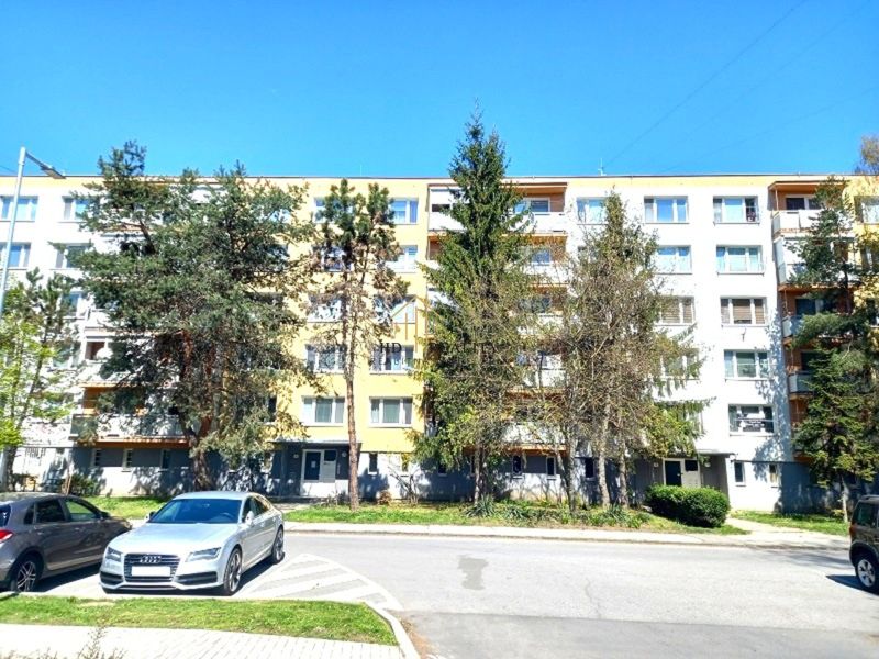 Apartment building in Fiľakovo, exterior with cars and greenery in front of a 4-room apartment.