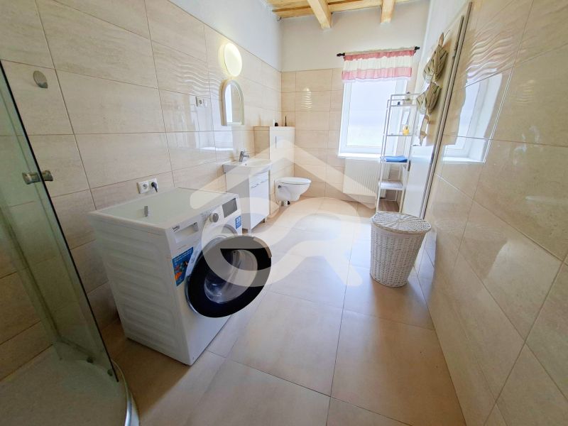 A bathroom in a family house with a washing machine, shower, and a window with a pink curtain.