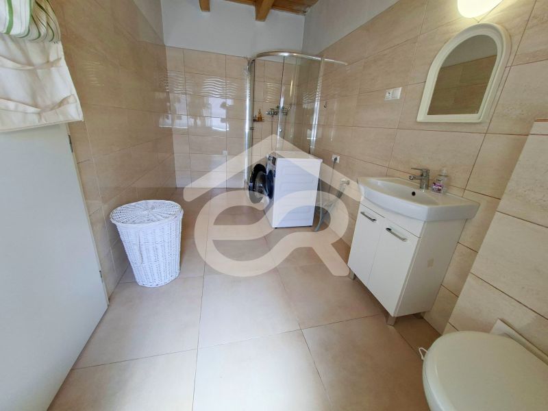 Bathroom in a family house with a washing machine and a shower, light tiles.