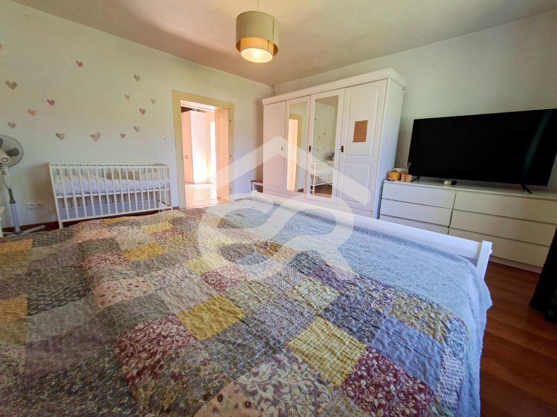 A bedroom with a wood-patterned floor in a family house, with a large bed and a baby crib.