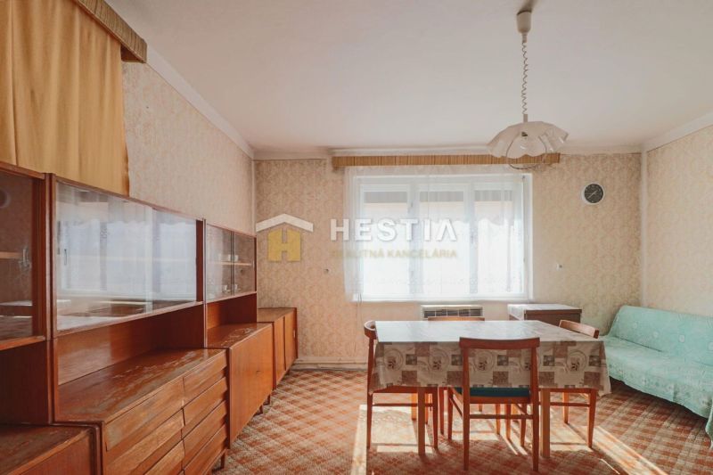 A dining room in a family house with retro furniture and a carpet, dominated by a bright window.
