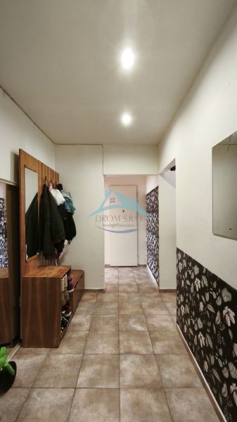 A hallway in a 2-room apartment with tiled flooring and floral patterned wallpaper.